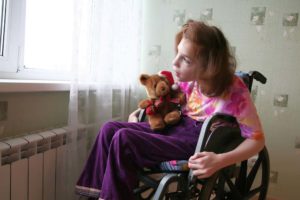 young girl holding a bear in a wheelchair