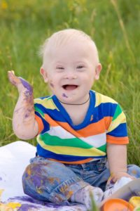 baby sitting in grass with paint on his arm and pants