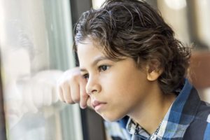 Pensive Latino little boy looking through a window