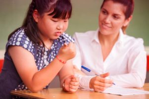 teacher holding pen working with young girl