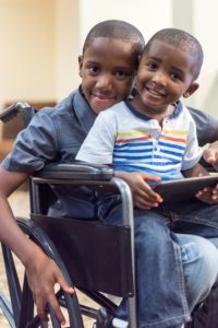 Black/African-American smiling child in a wheelchair playing with his little brother