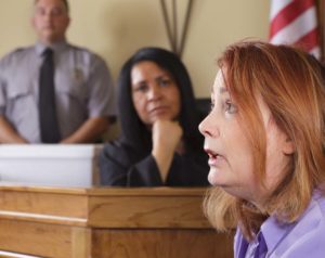 A witness in a courtroom with the judge in the out-of-focus background.