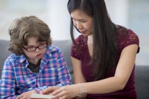 An elementary-aged boy practices reading with a teacher. The child has a tracheostomy.