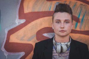 Young person wearing headphones standing in front of some graffiti