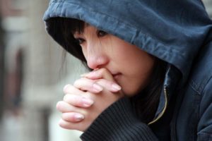 Teenage Asian girl wearing hoodie with clasped hands to her face.