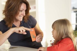 teacher working with young girl while holding a flashcard