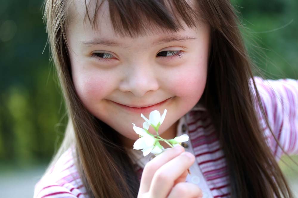 Young white girl with down syndrome girl holding a flower and smiling.