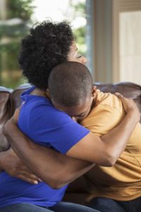 Black/African-American mother hugging her teenage son, his head on her shoulder.