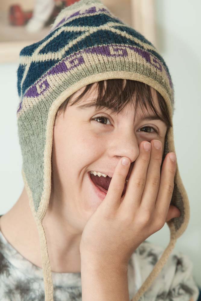 young boy with knit hat laughing and covering his face with his hand