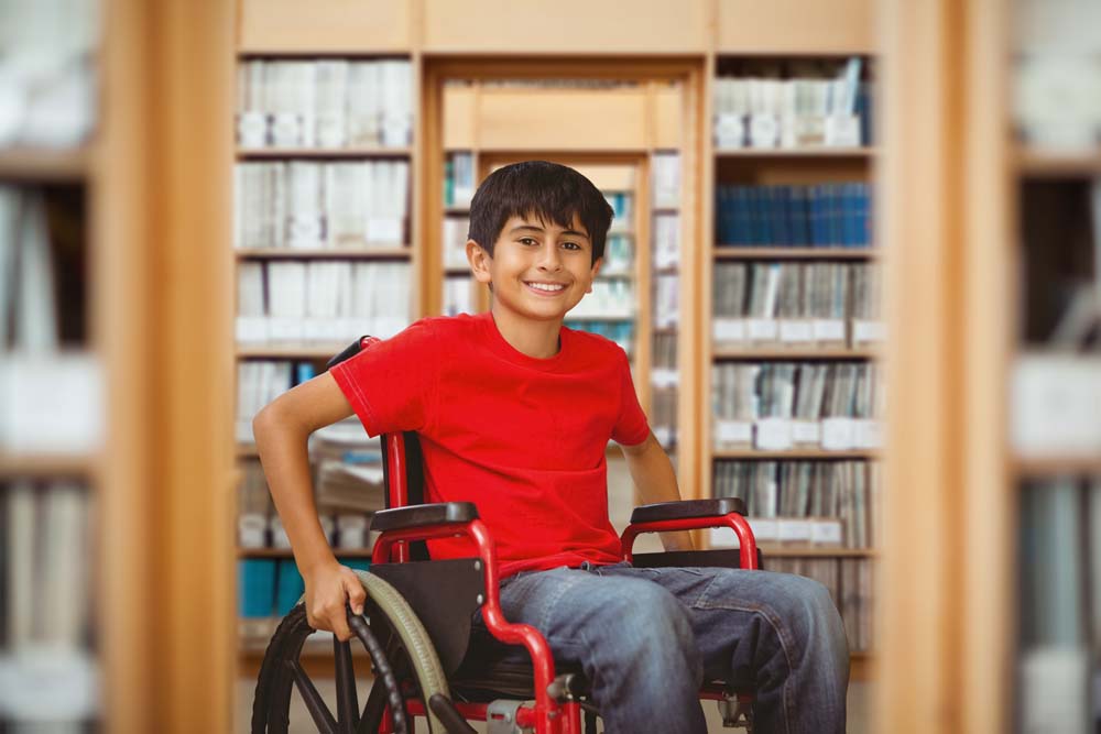 young smiling Latino boy in a wheelchair in a libary