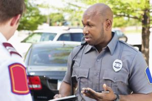 Black/African-American police officer interrogating people at an emergency scene.