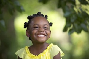 Black/African-American preschooler in bright yellow top grins happily.