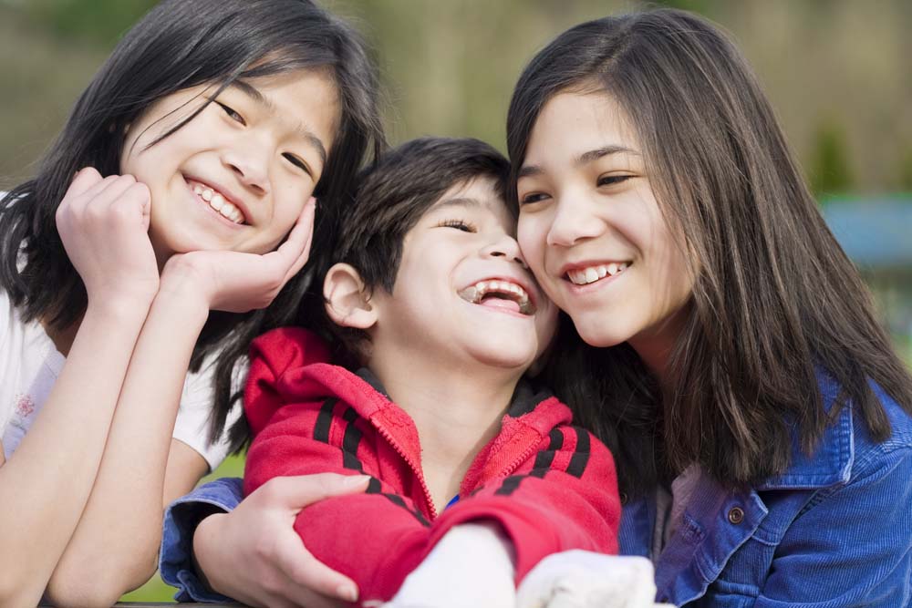 Two older Asian sisters cuddle with a younger brother with a disability.