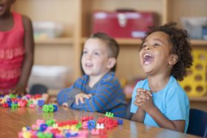 A multi-ethnic group of elementary age children are playing with toy blocks together at a table.