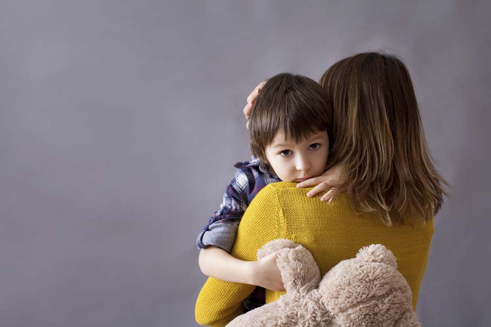 Sad little child, boy, hugging his mother, stuffed bear in his hand.