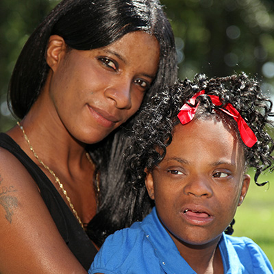A Black/African-American mom stands with her daughter with a disability.